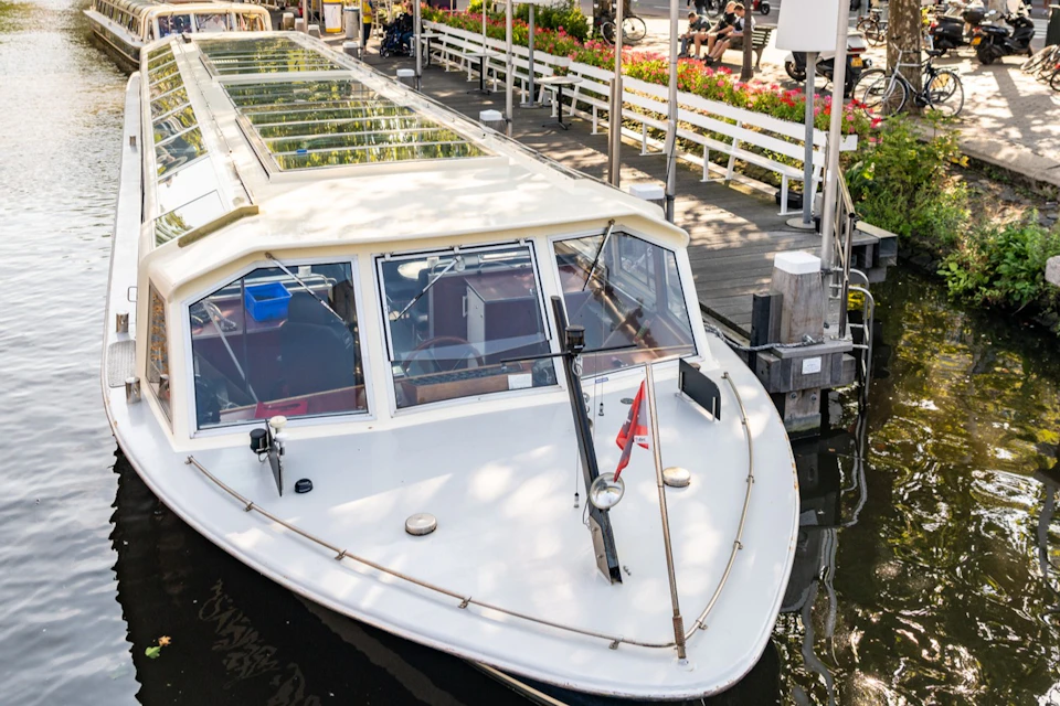 A white canal boat docked by a wooden pier with flowers and a street in the background.