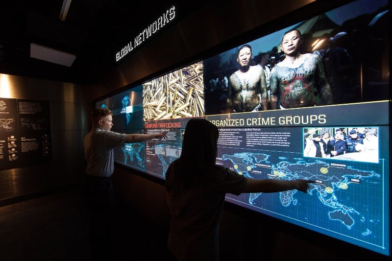 Person interacts with a large digital display about organized crime groups, featuring images of men, bullets, and a world map.