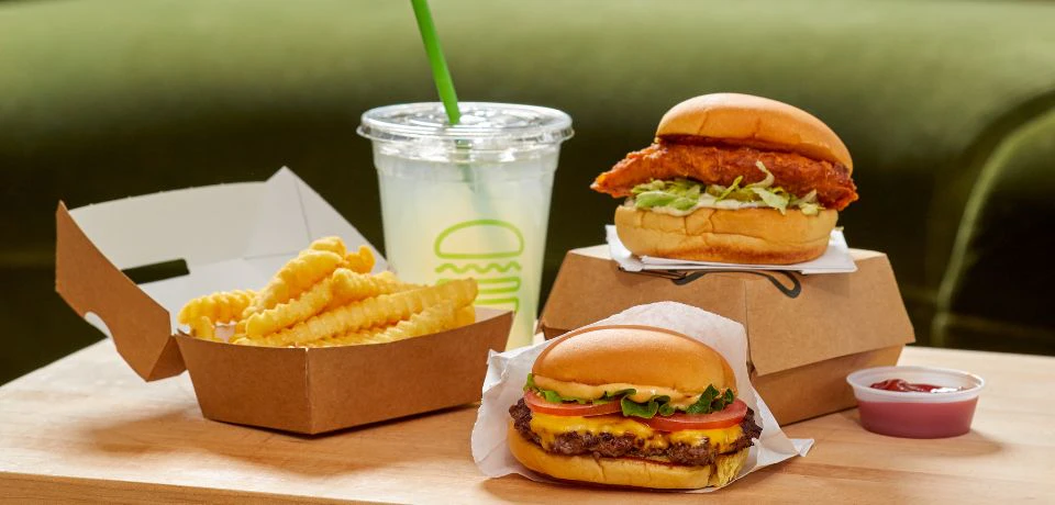 A meal with crinkle-cut fries, a burger with toppings, a chicken sandwich, and a cup of lemonade with a green straw.