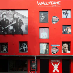 Röd byggnadsfasad med flera fönster som visar svartvita bilder av musiker. Text om byggnaden: "Wall of Fame Dublin."