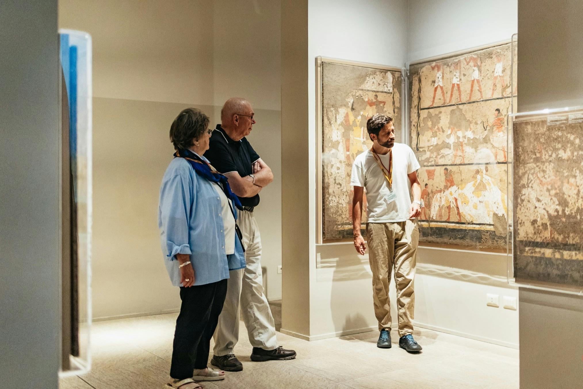 A guide explains ancient wall paintings to three visitors in a museum setting.