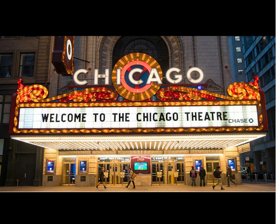 The illuminated marquee of the Chicago Theatre displays the message "Welcome to the Chicago Theatre" with people walking below.