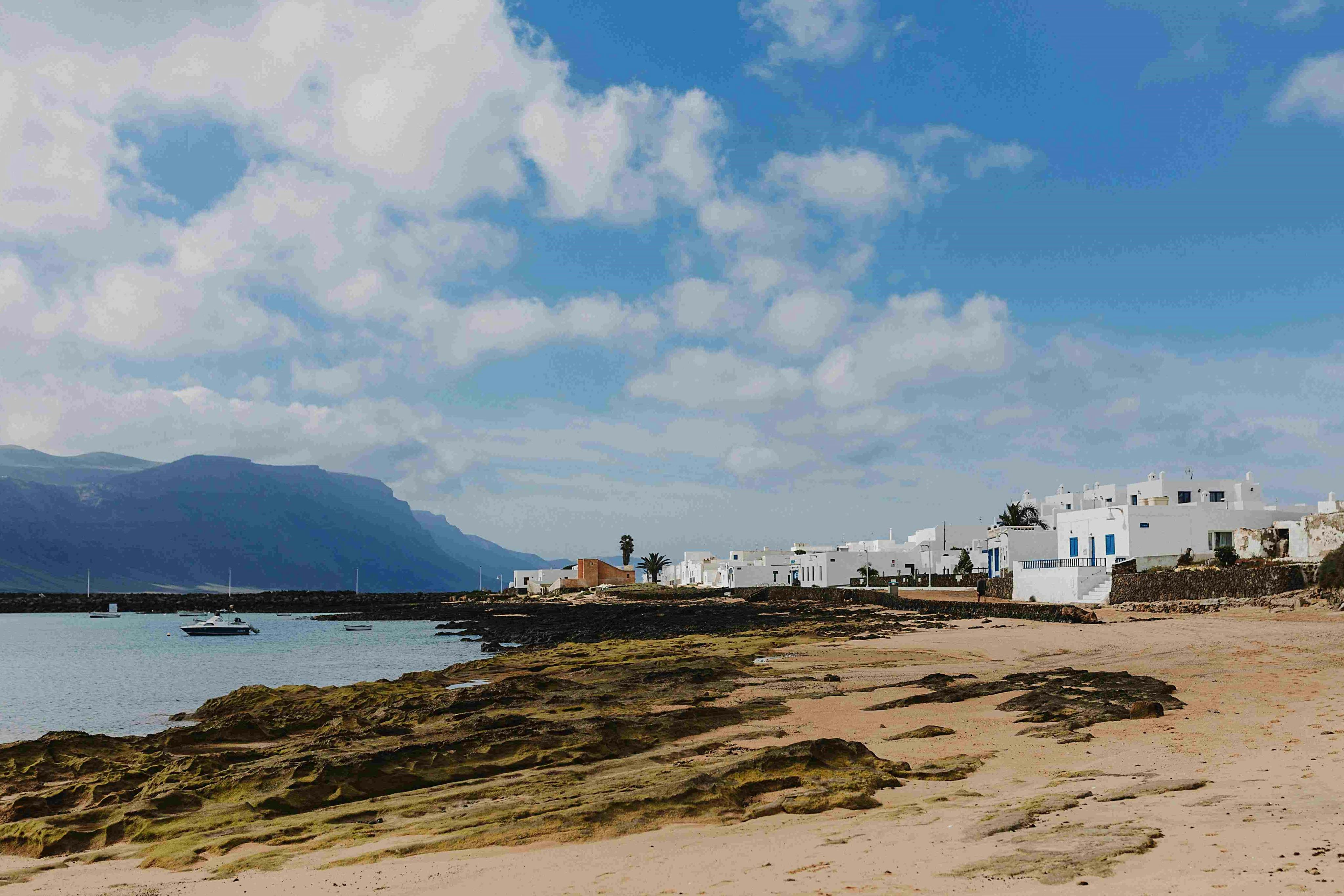 在一片多云的天空下，岩石海岸线上有白色的建筑物和一座山脉。