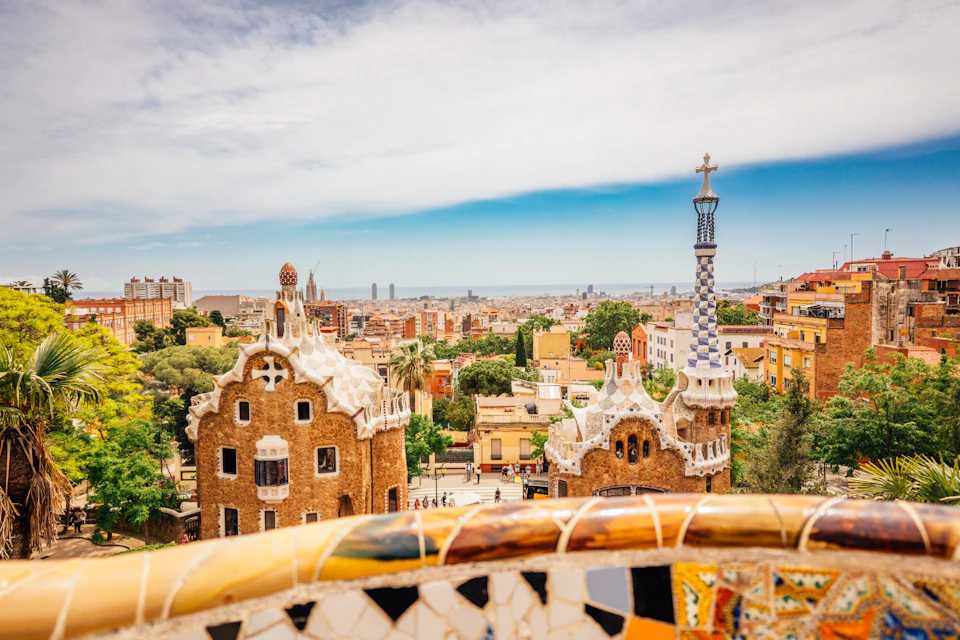 A colorful cityscape with unique ceramic-adorned buildings and a view of a distant skyline under a blue sky.