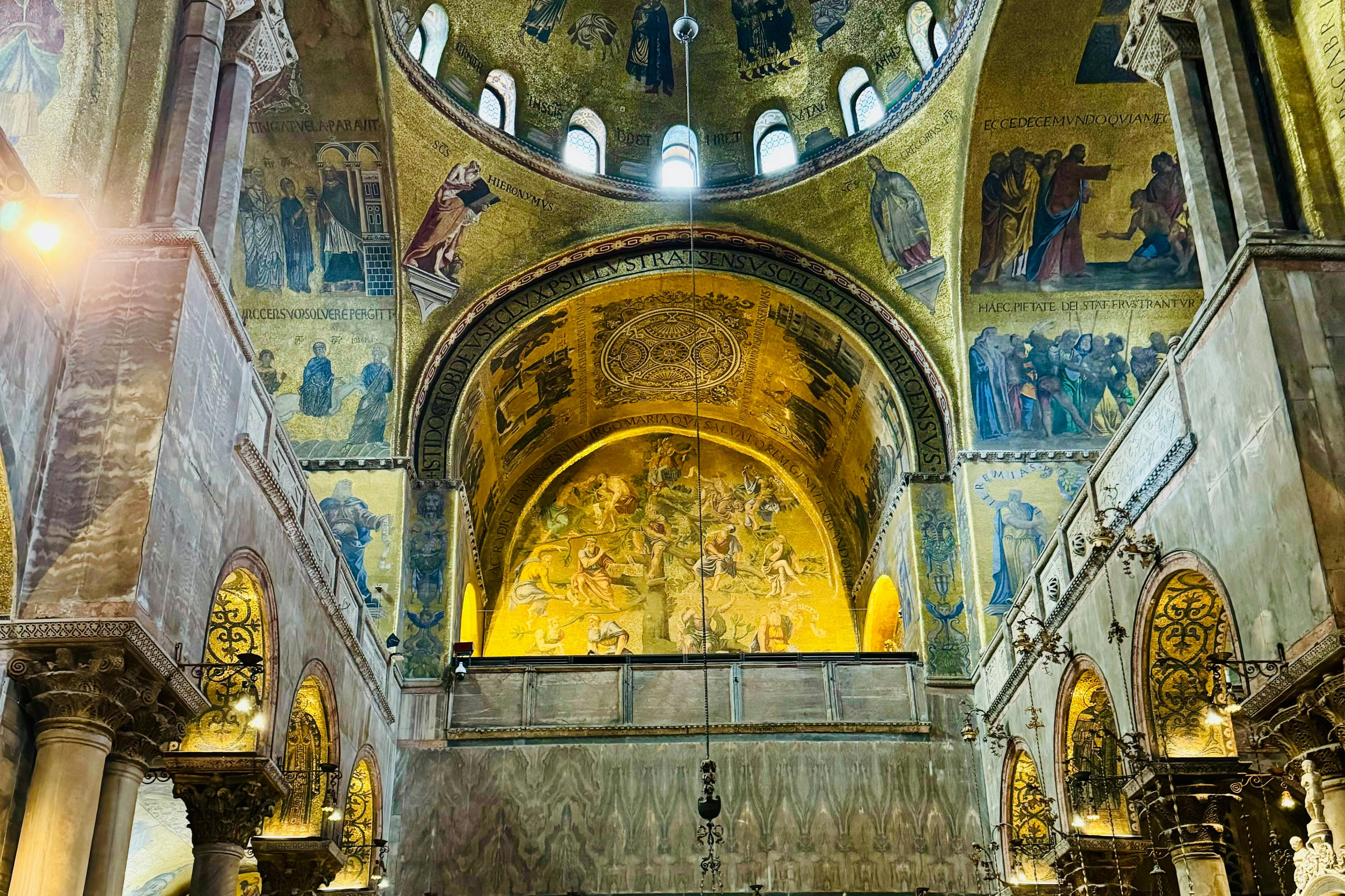 Interior of a richly decorated church with detailed golden mosaics and arched ceilings adorned with religious scenes.