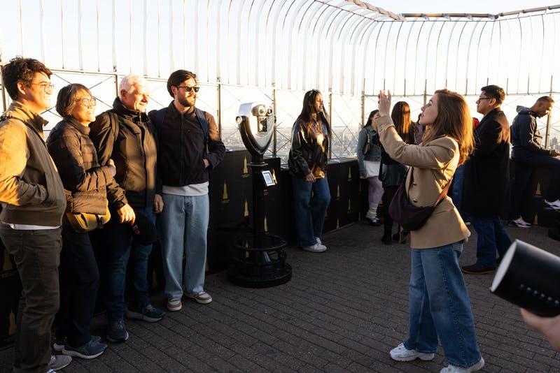 En gruppe mennesker, der poserer for et billede på et observationsdæk i nærheden af en møntbetjent søger på en klar dag.