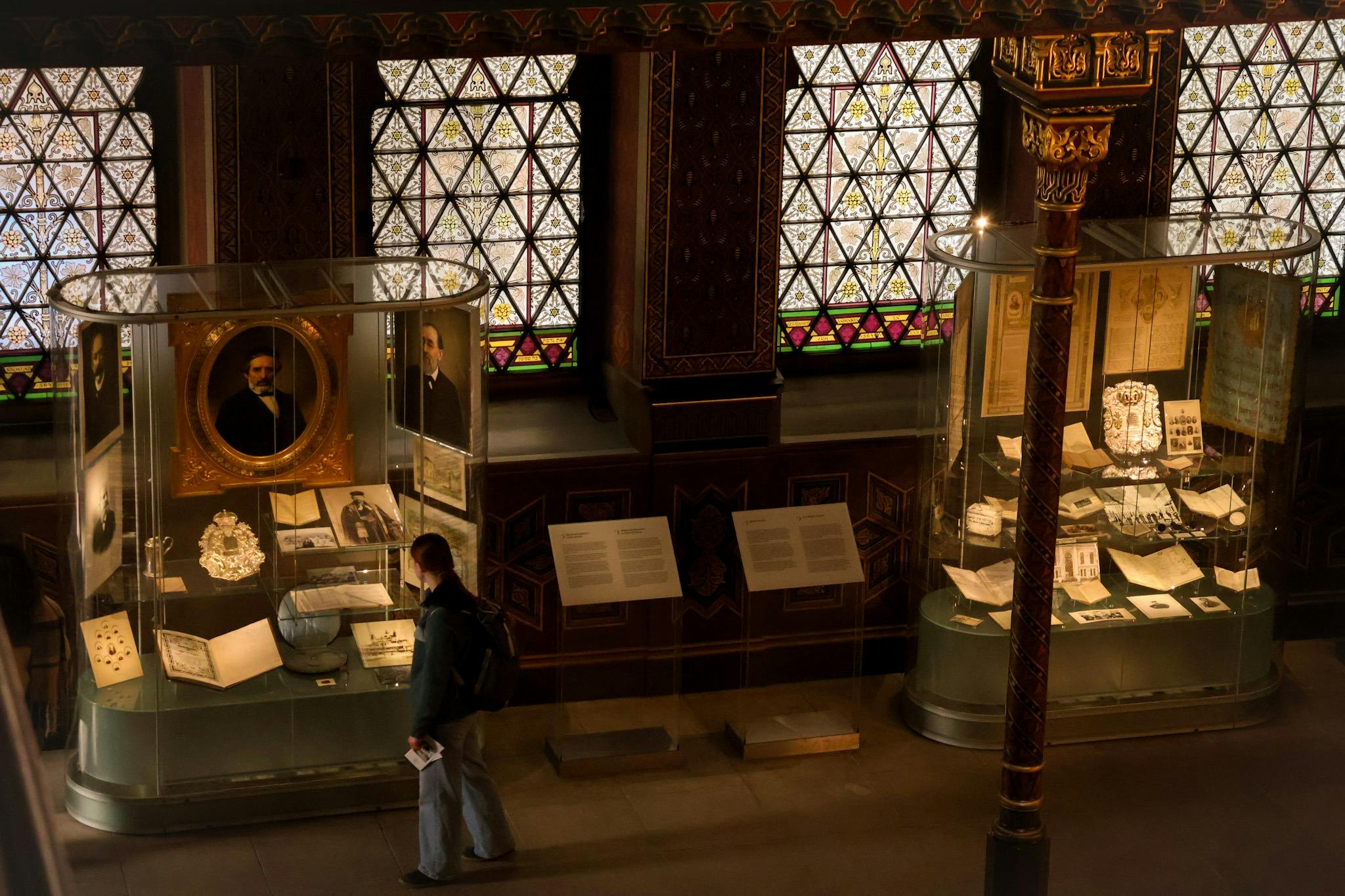 A person observes exhibits in a museum with ornate stained glass windows and detailed interior decorations.