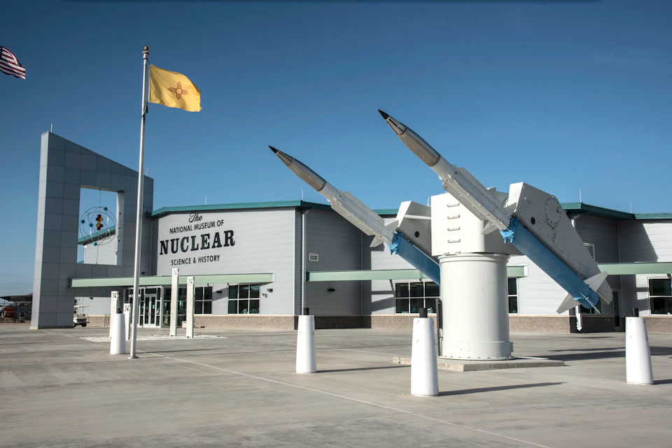 Exterior of The National Museum of Nuclear Science & History, featuring missile exhibits and a flagpole with a yellow flag.