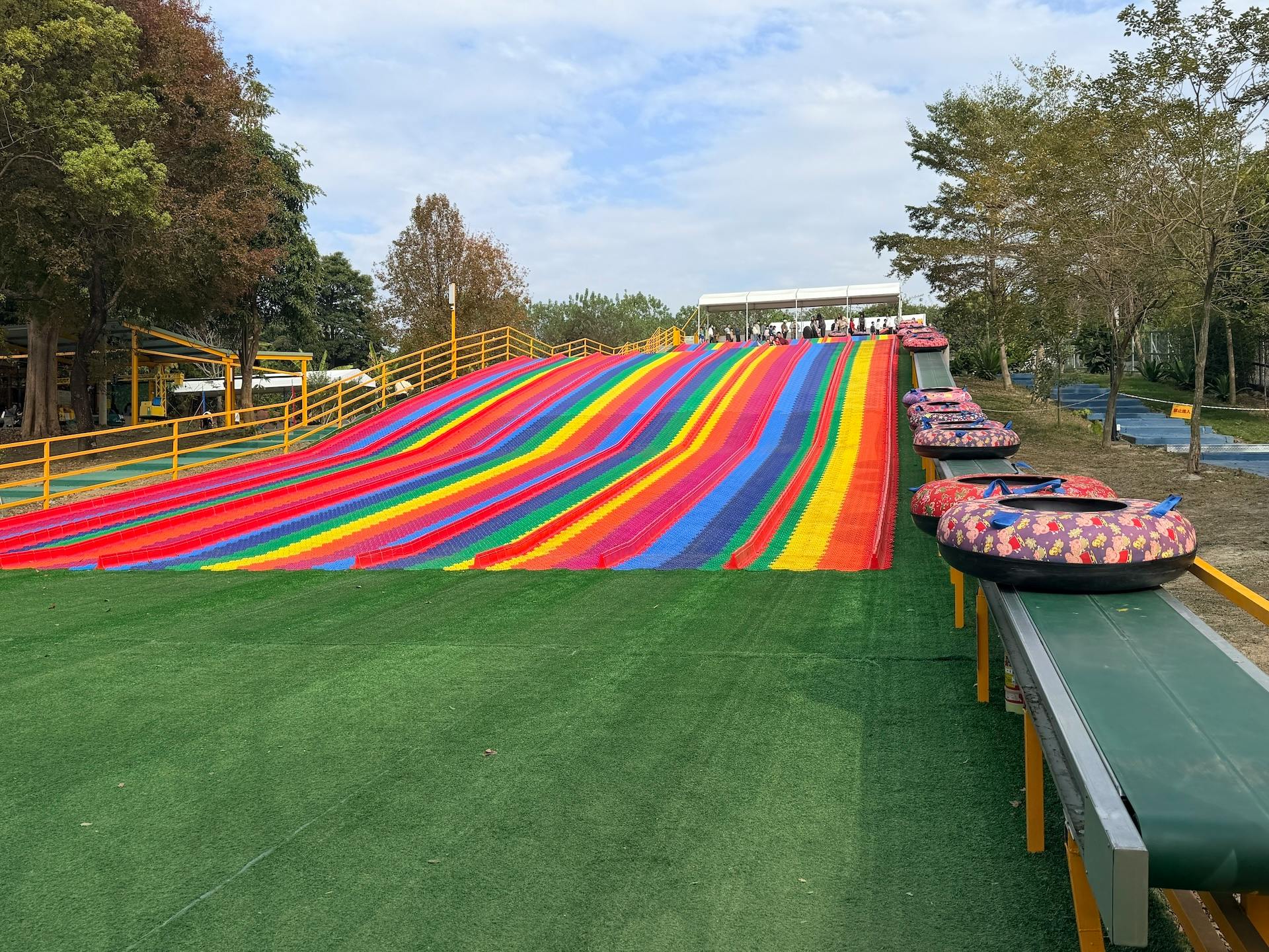 A colorful slide with multiple lanes and inflatable tubes on a grass-like surface, with trees in the background.