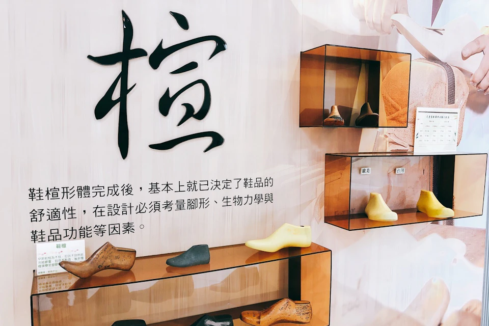 Display of shoe models and wooden lasts on shelves, with text in Chinese and a large decorative character on the wall.