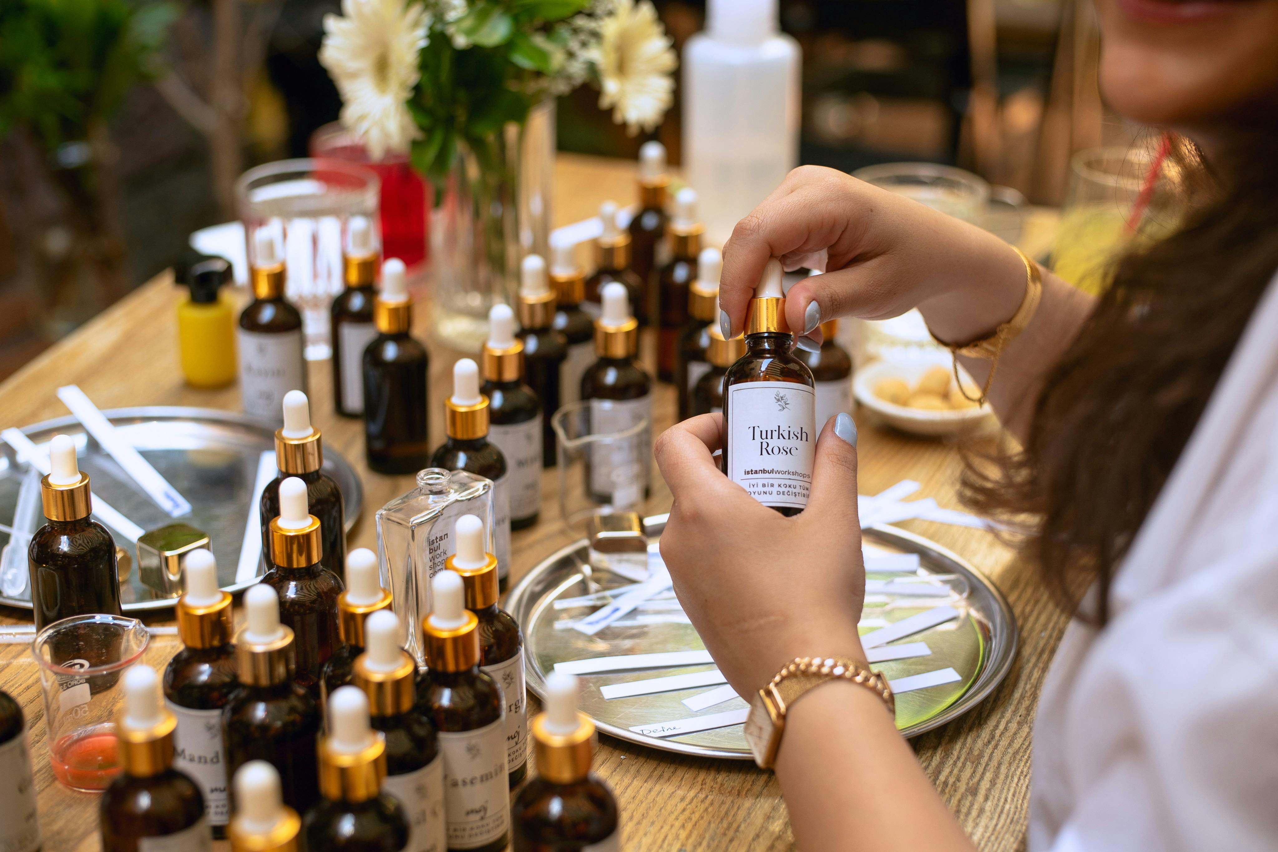 Close-up of hands holding a bottle labeled "Turkish Rose" among various perfume ingredients on a table.