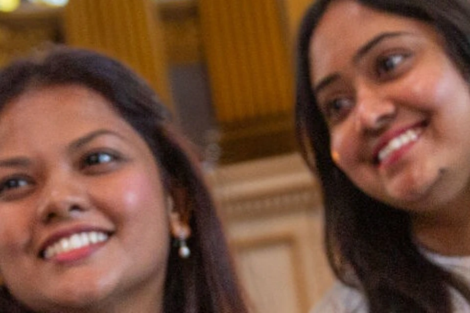 Two women smiling and taking a selfie inside a church with stained glass windows and ornate decor in the background.