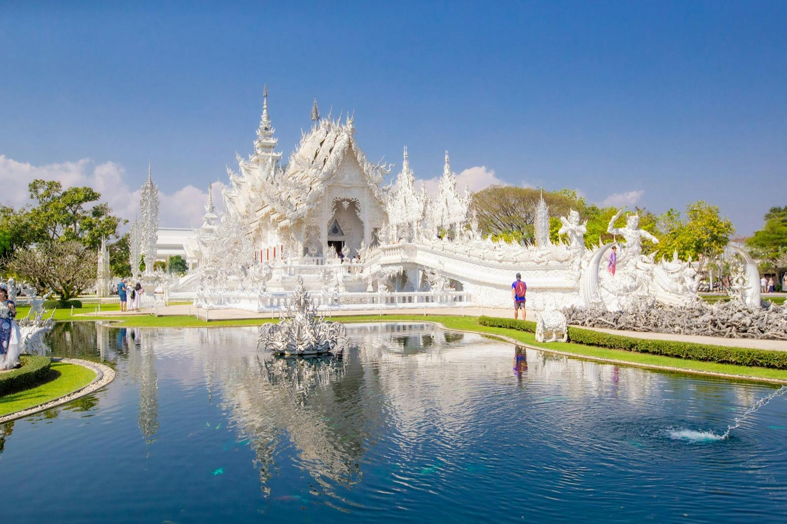 Ein weißer verschnörkelter Tempel mit komplizierten Details, ein Reflexionsbecken im Vordergrund und ein klarer blauer Himmel im Hintergrund.