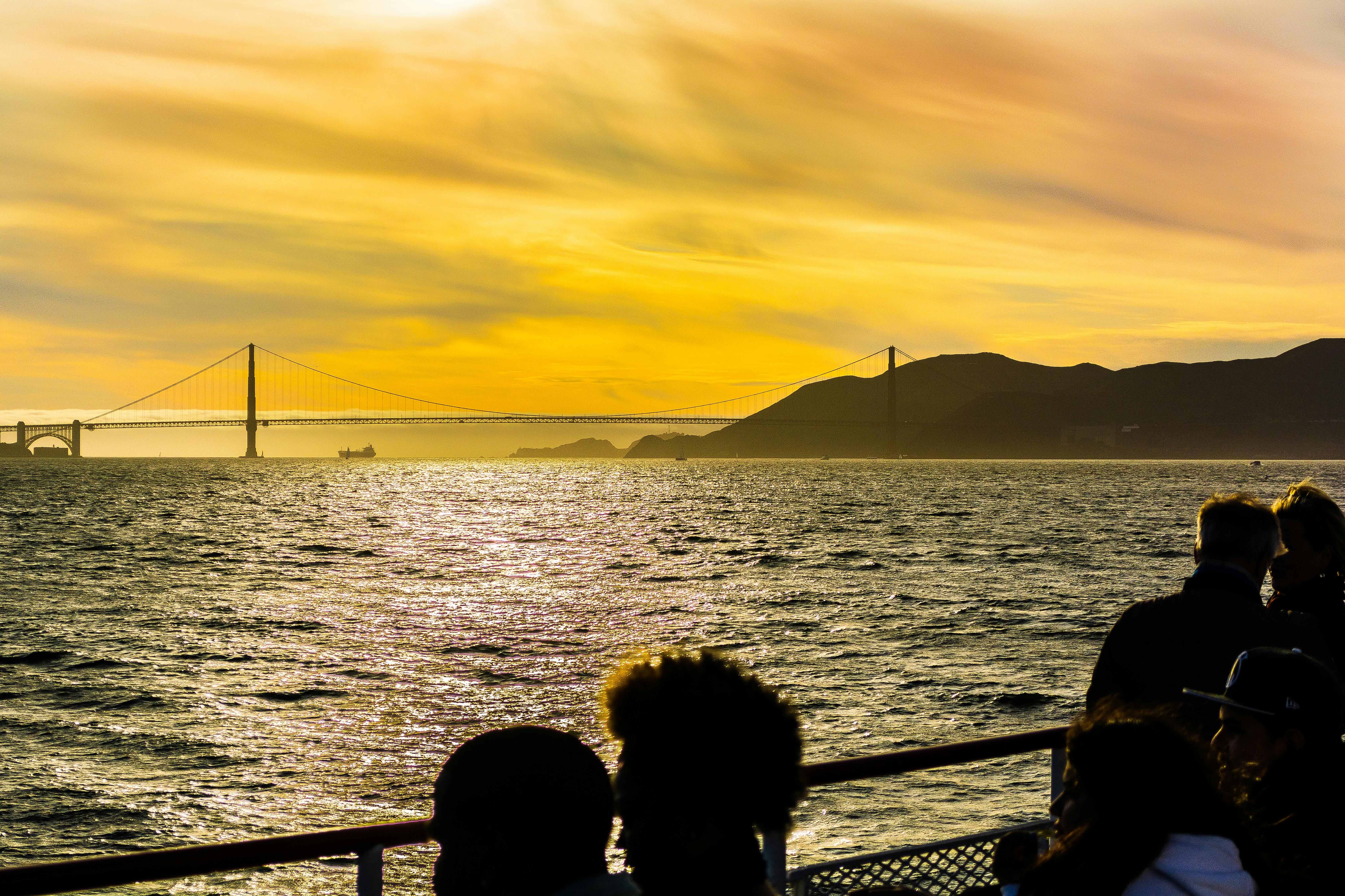 Ponte Golden Gate ao pôr do sol, vista de um barco com pessoas em silhueta em primeiro plano.