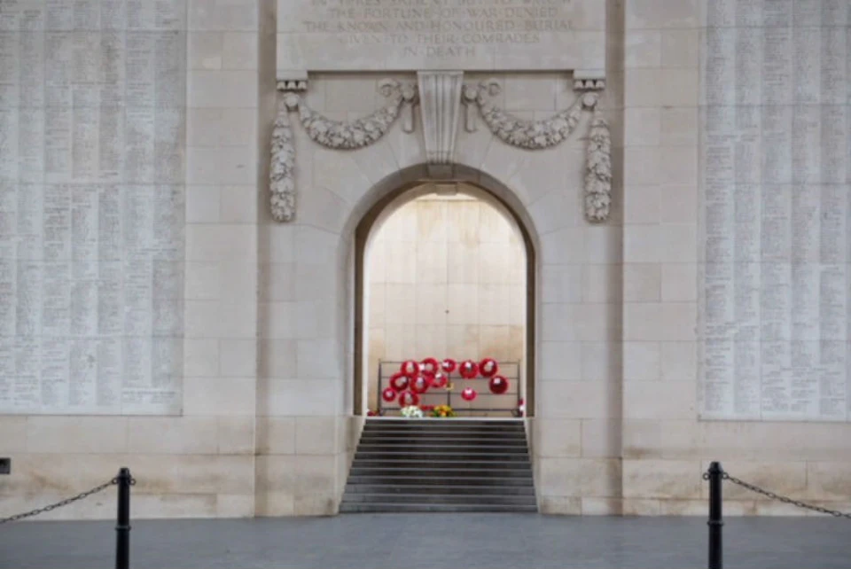 Stone archway with decorative carvings, leading to steps adorned with red wreaths and bouquets against a pale background.