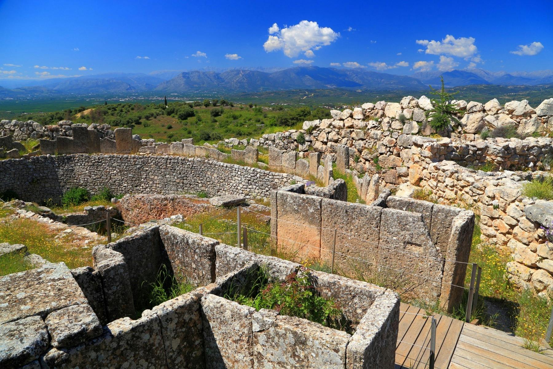 Ancient stone graves arranged in a circular enclosure with views of green hills and distant mountains.