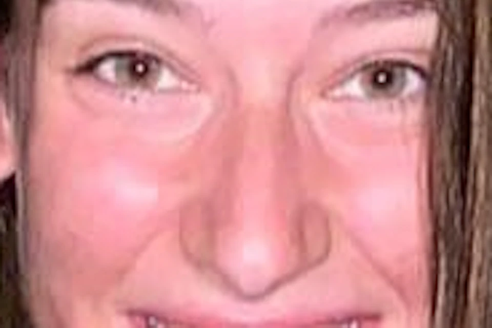 A person crouches and smiles inside a narrow, cylindrical tunnel with rough, textured walls. They are wearing a green tank top and denim shorts.