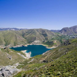 En turkos sjö omgiven av gröna kullar och berg under en klarblå himmel.