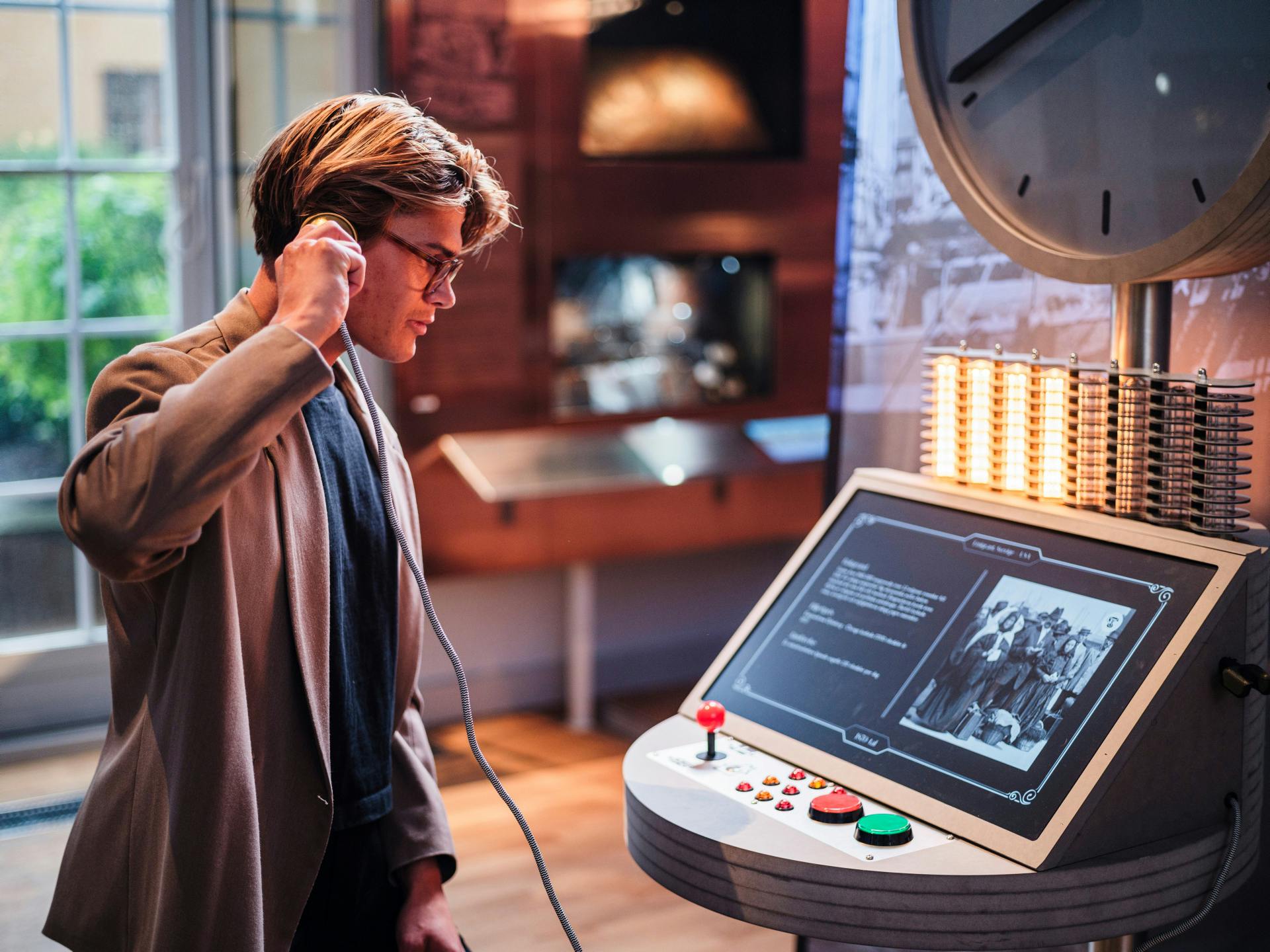 Eine Person hält einen Telefonhörer in der Hand und interagiert mit einem Ausstellungsstück in einer museumsähnlichen Umgebung.