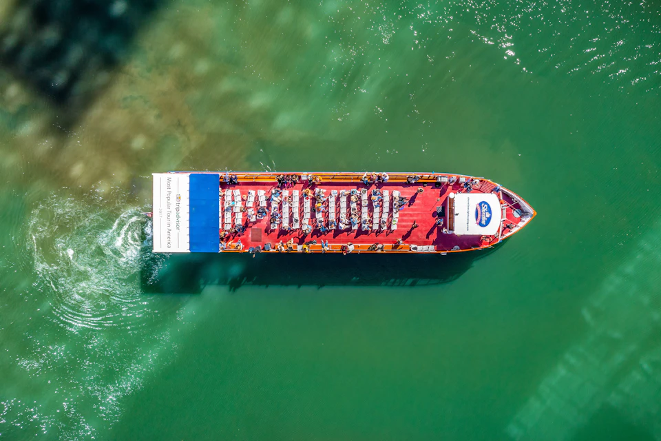 Aerial view of a red sightseeing boat with passengers seated, cruising on green water.