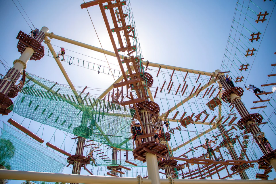 Many people navigating a high ropes course with various wooden and rope bridges against a clear blue sky.