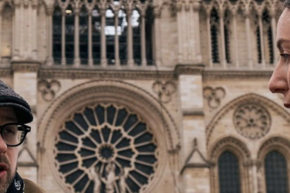 Two people talking in front of a gothic cathedral with ornate architecture and large rose window.