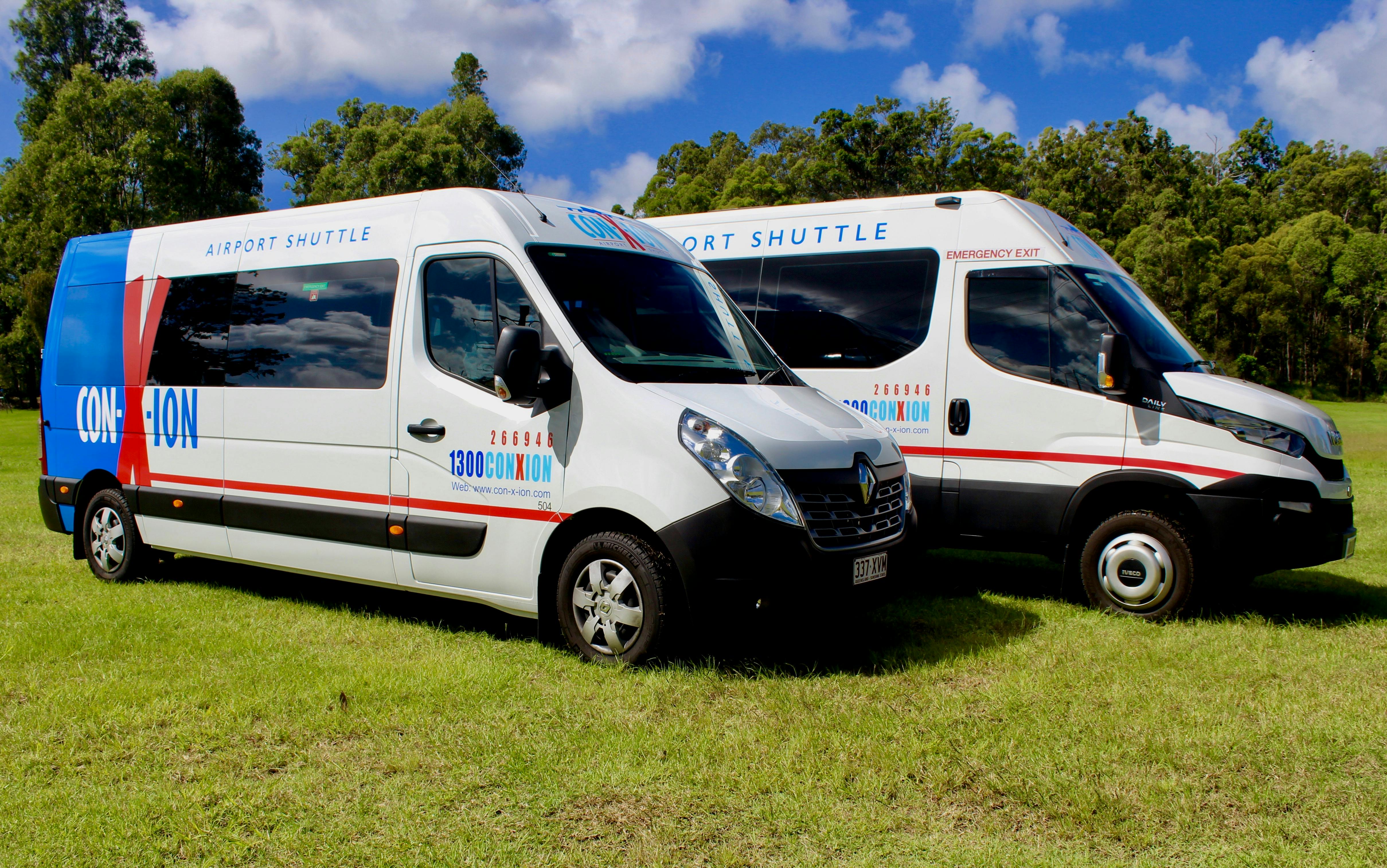 Due furgoni navetta bianchi con il brand "100% ConXion", parcheggiati sull'erba sotto un cielo parzialmente nuvoloso.