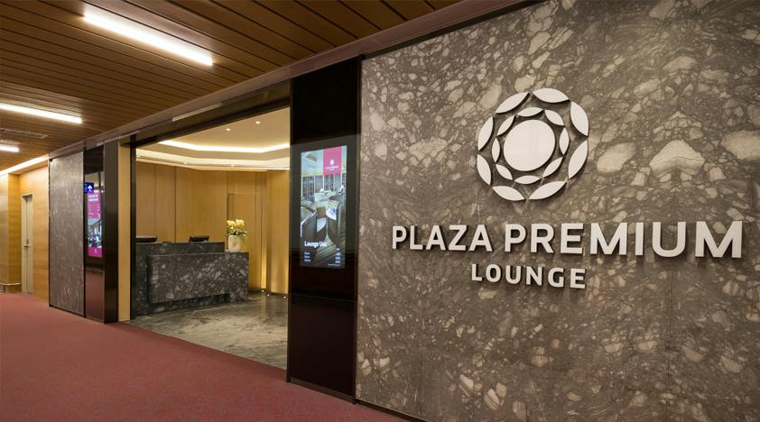 Entrance of the Plaza Premium Lounge with a marble wall, logo, and reception desk visible inside.