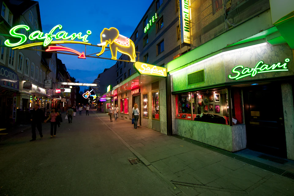 Night scene of a city street with neon signs, including a large yellow elephant, and people walking by shops and buildings.
