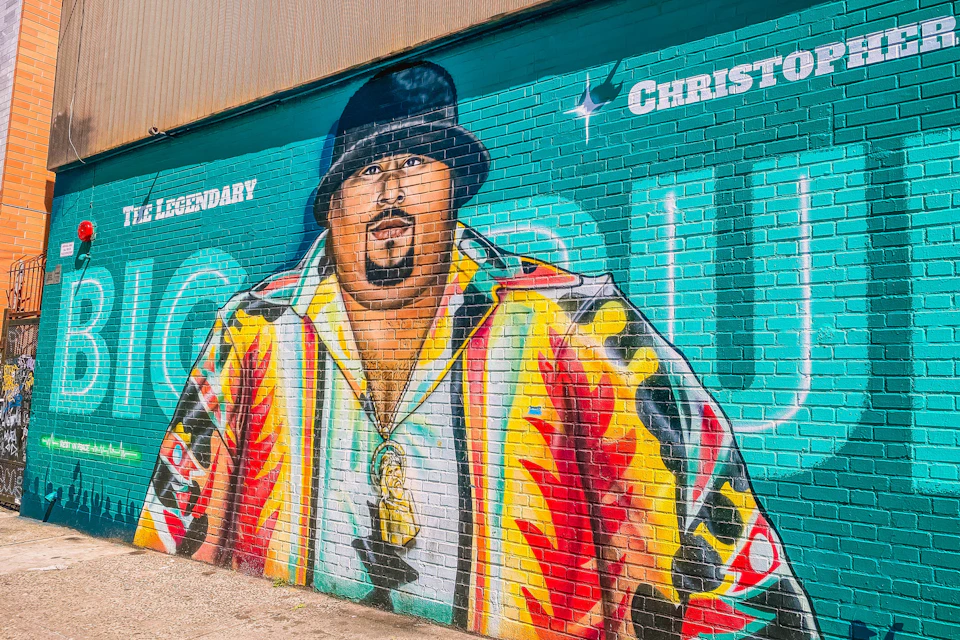 Colorful mural of a man wearing a vibrant shirt and black hat, with text saying "Legendary" and "Christopher" on a brick wall.