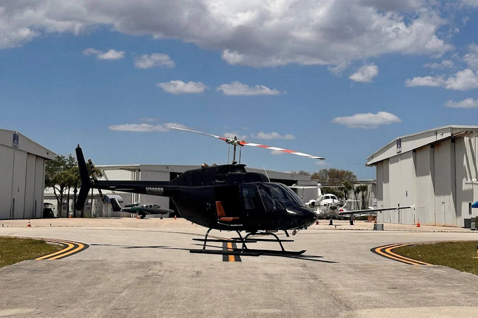 A black helicopter is parked on a tarmac between hangars under a partly cloudy sky.