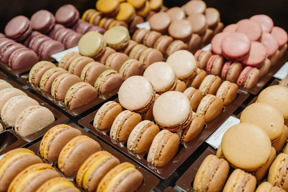 Assorted colorful macarons displayed in rows on trays, arranged by flavor and color.