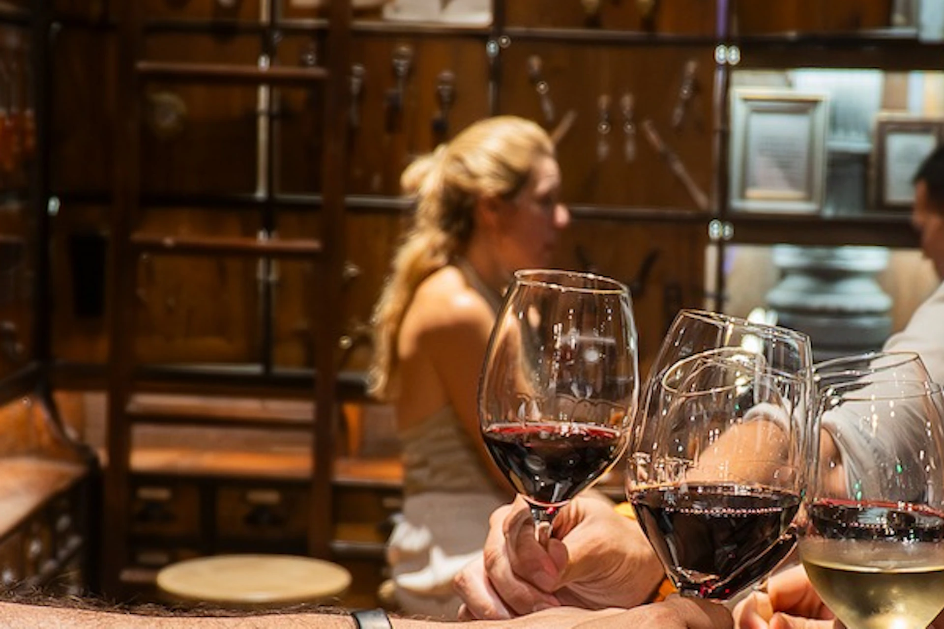 A group of people clinking wine glasses in a cozy restaurant, with a wooden wall and shelves filled with items in the background.