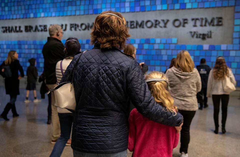 A group of people, including an adult and child in the foreground, view a blue-tiled wall with visible text.