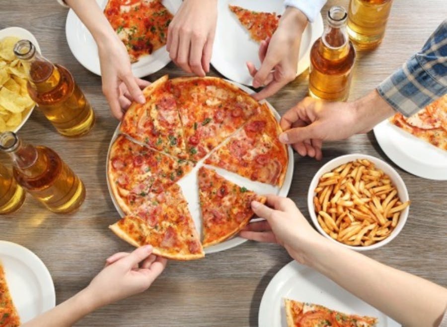 Six hands reaching for slices of pizza on a table with fries and beer.