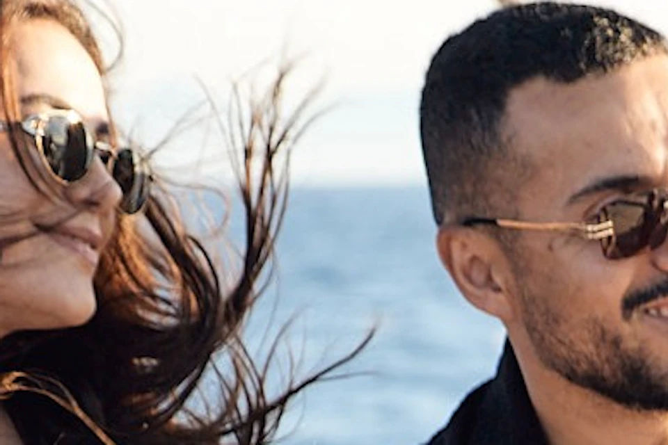 Four people enjoying a sunny day on a boat, with wind blowing their hair, against a backdrop of a calm sea.