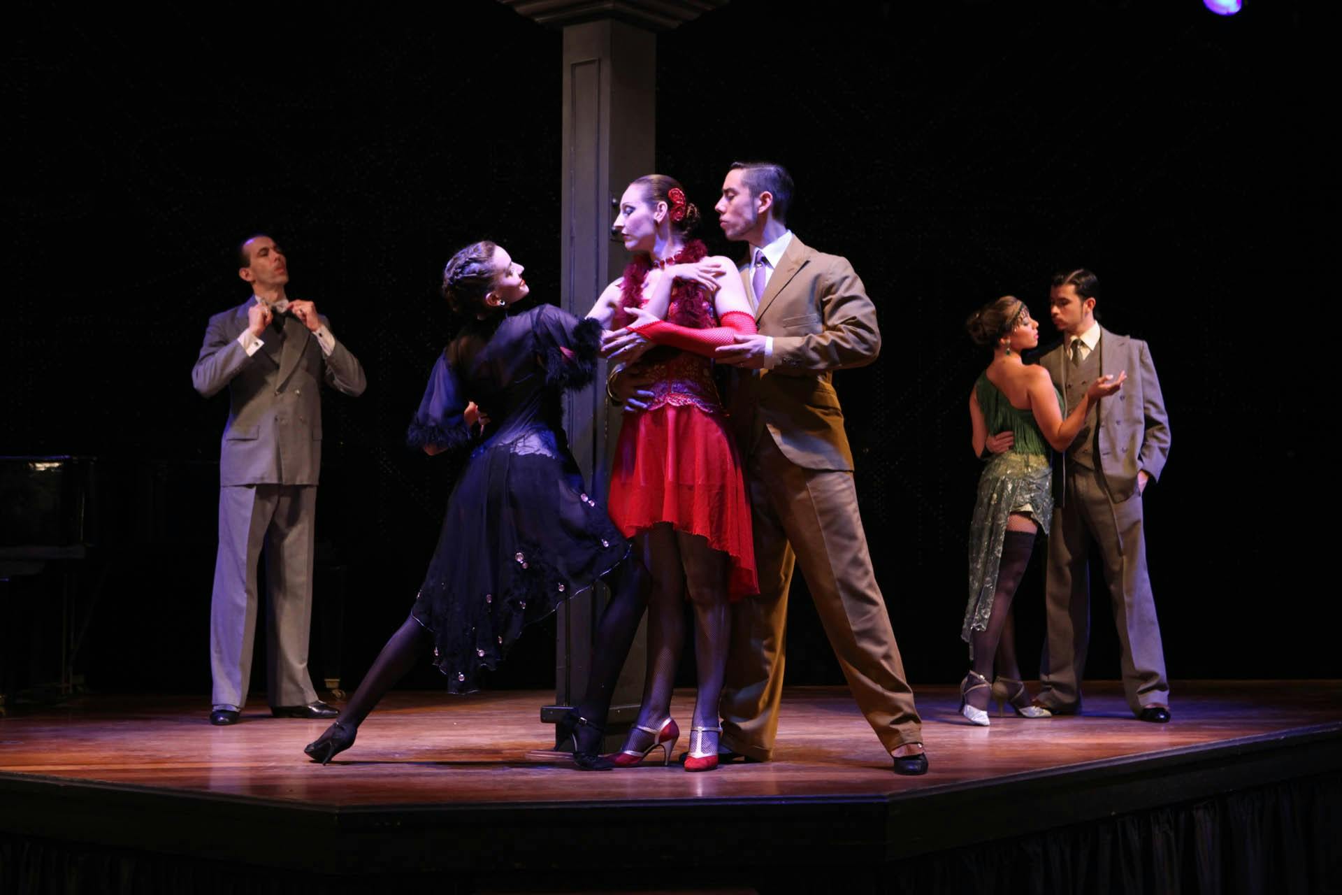 Four couples in elegant 1920s-style attire dance on a stage against a dark backdrop.