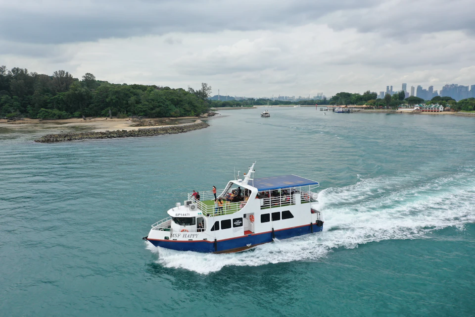 A passenger ferry labeled "Rise Happy" sailing on a calm waterway, with lush greenery and a cloudy sky in the background.