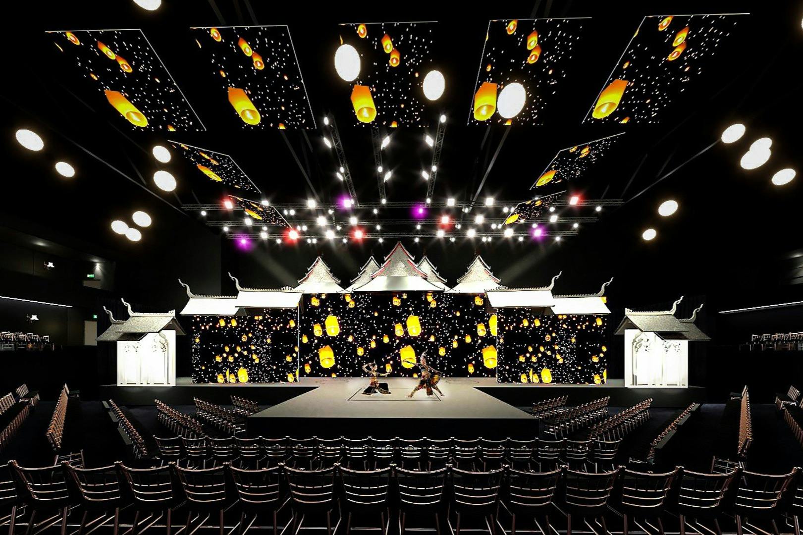 Un grande palcoscenico con proiezioni di lanterne su schermi, strutture tradizionali sul tetto, luci luminose in alto e file di sedie vuote.
