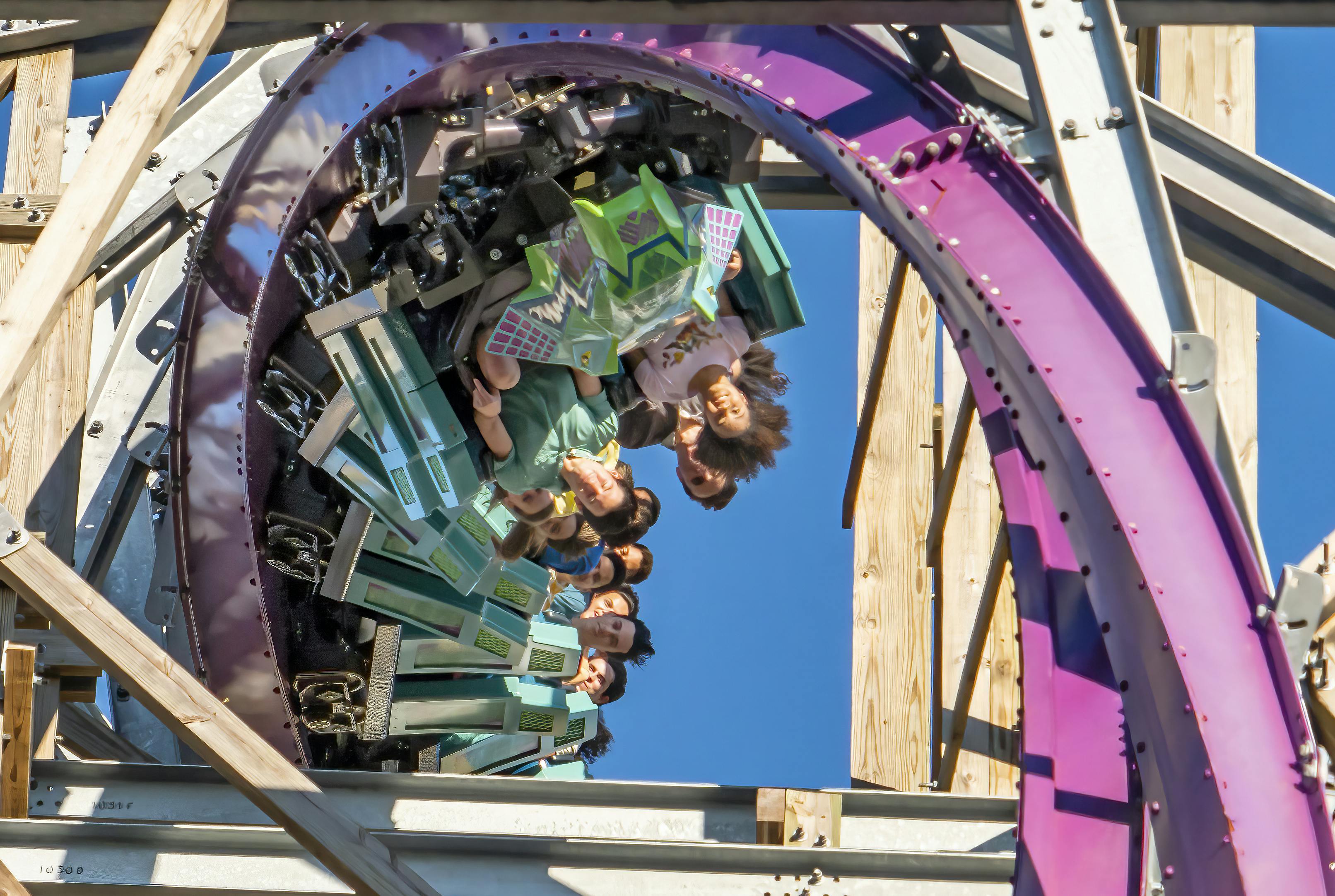 晴れた青い空を背景に、垂直ループで逆さまに走るジェットコースターのライダーたち。