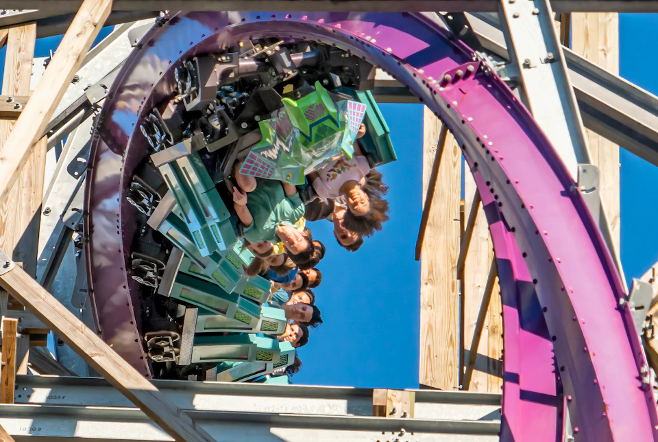 Rollercoaster riders upside down on a vertical loop, with a clear blue sky in the background.