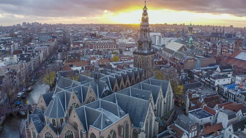 Aerial view of a historic city with a prominent Gothic-style church and bell tower at sunset. Urban landscape with rooftops and buildings.