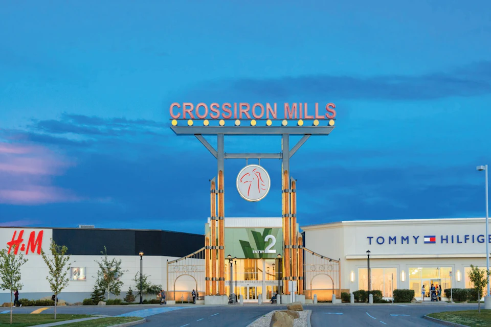 CrossIron Mills shopping center entrance with a large sign and surrounding shops, including Tommy Hilfiger under a twilight sky.