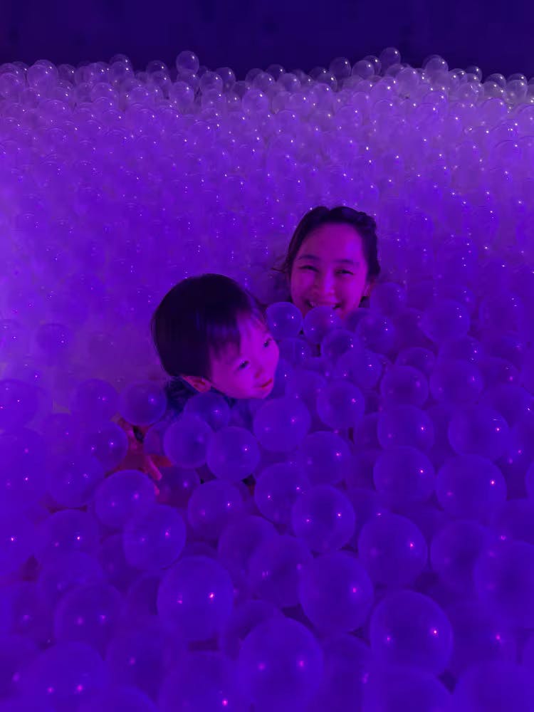 一位女士和一个孩子在紫色灯光下被半透明的球包围着微笑。