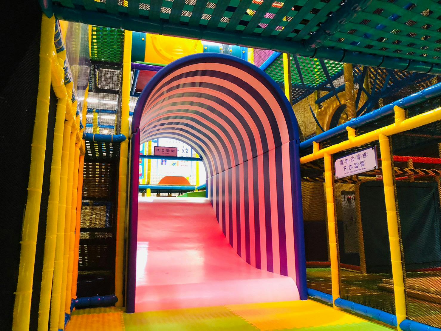 A colorful indoor playground with a striped tunnel slide and various climbing structures.
