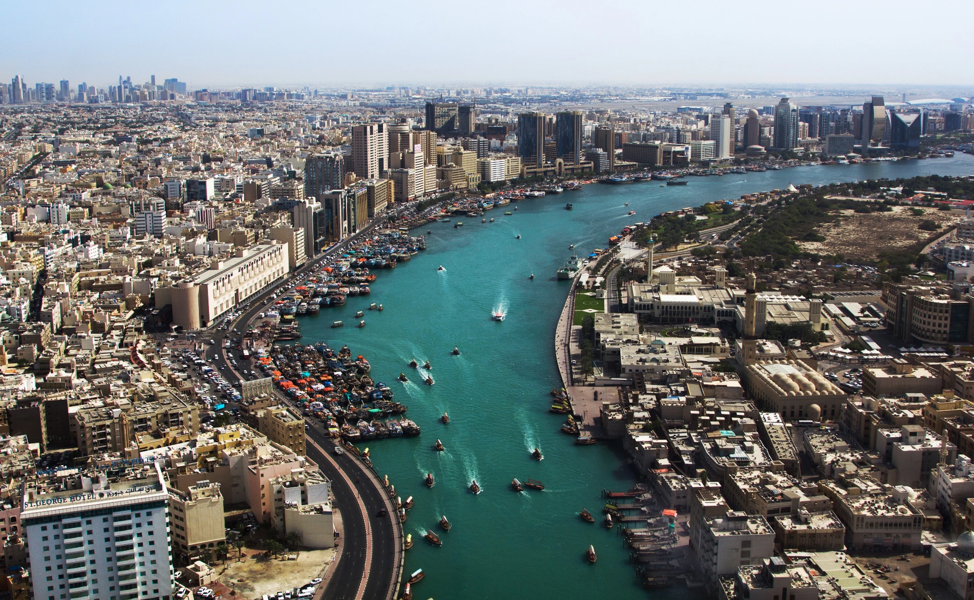 Aerial view of a cityscape with high-rise buildings, a river with boats, and densely packed structures on both banks.