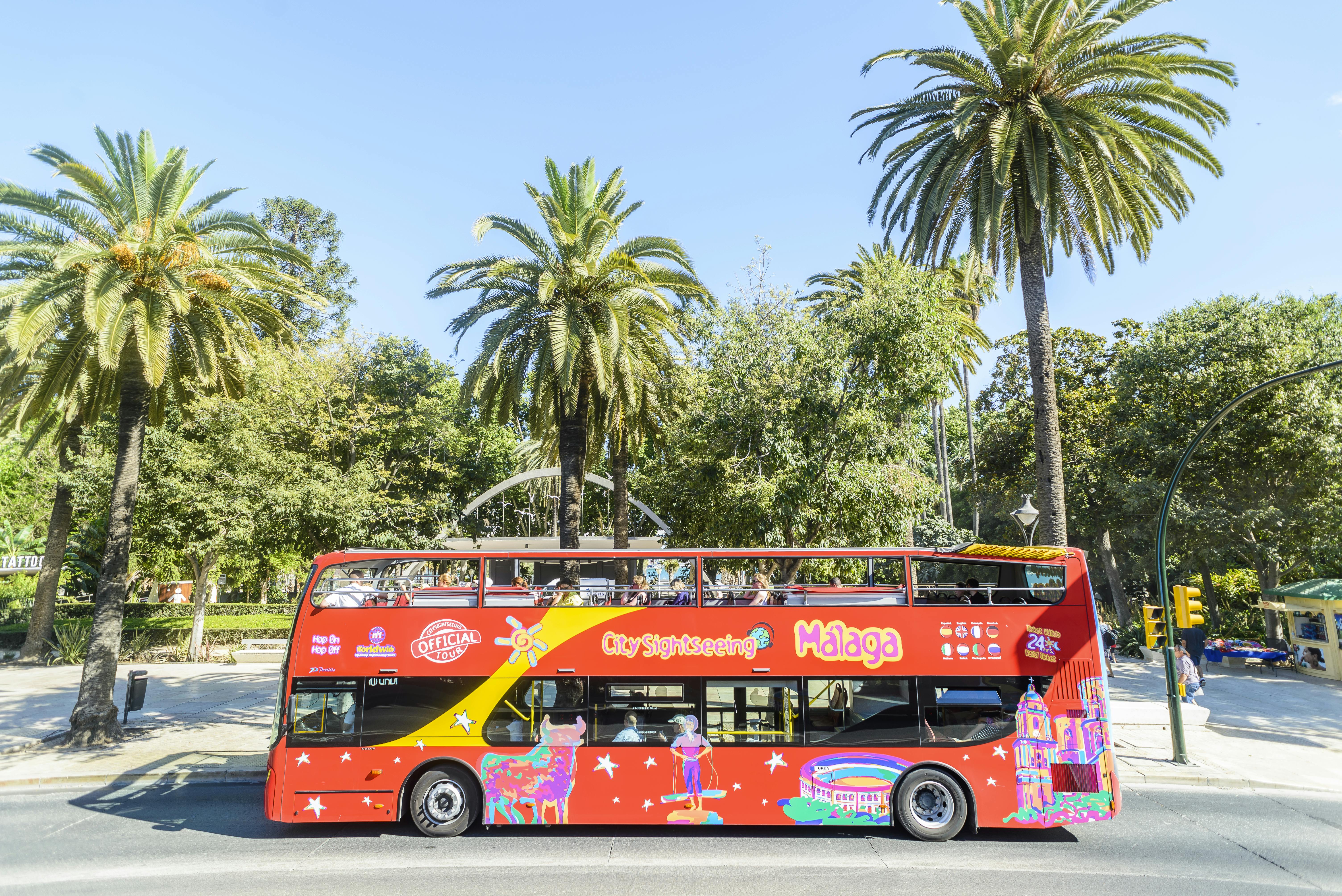 Červený dvoupatrový vyhlídkový autobus před palmami s nápisem „City Sightseeing Málaga“ na boku.