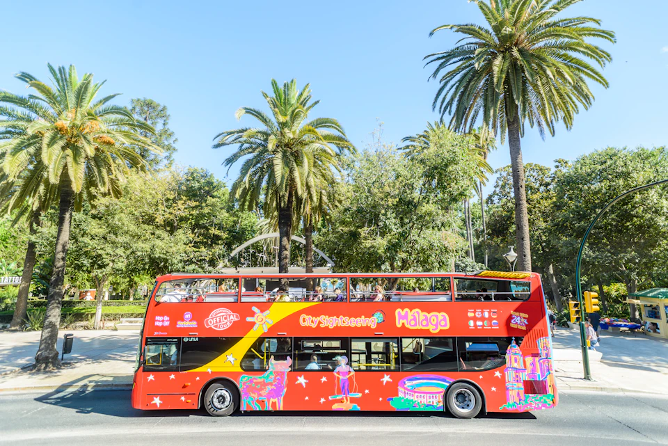 Red double-decker sightseeing bus in front of palm trees, with "City Sightseeing Málaga" written on the side.