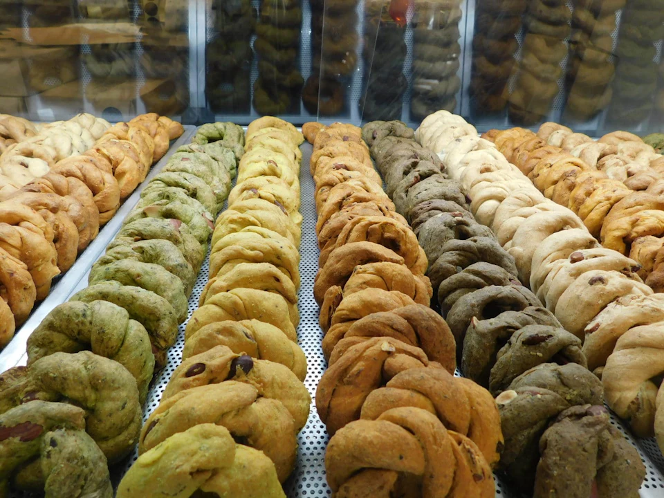 Rows of twisted breadsticks in green, yellow, brown, and beige arranged in a display case.
