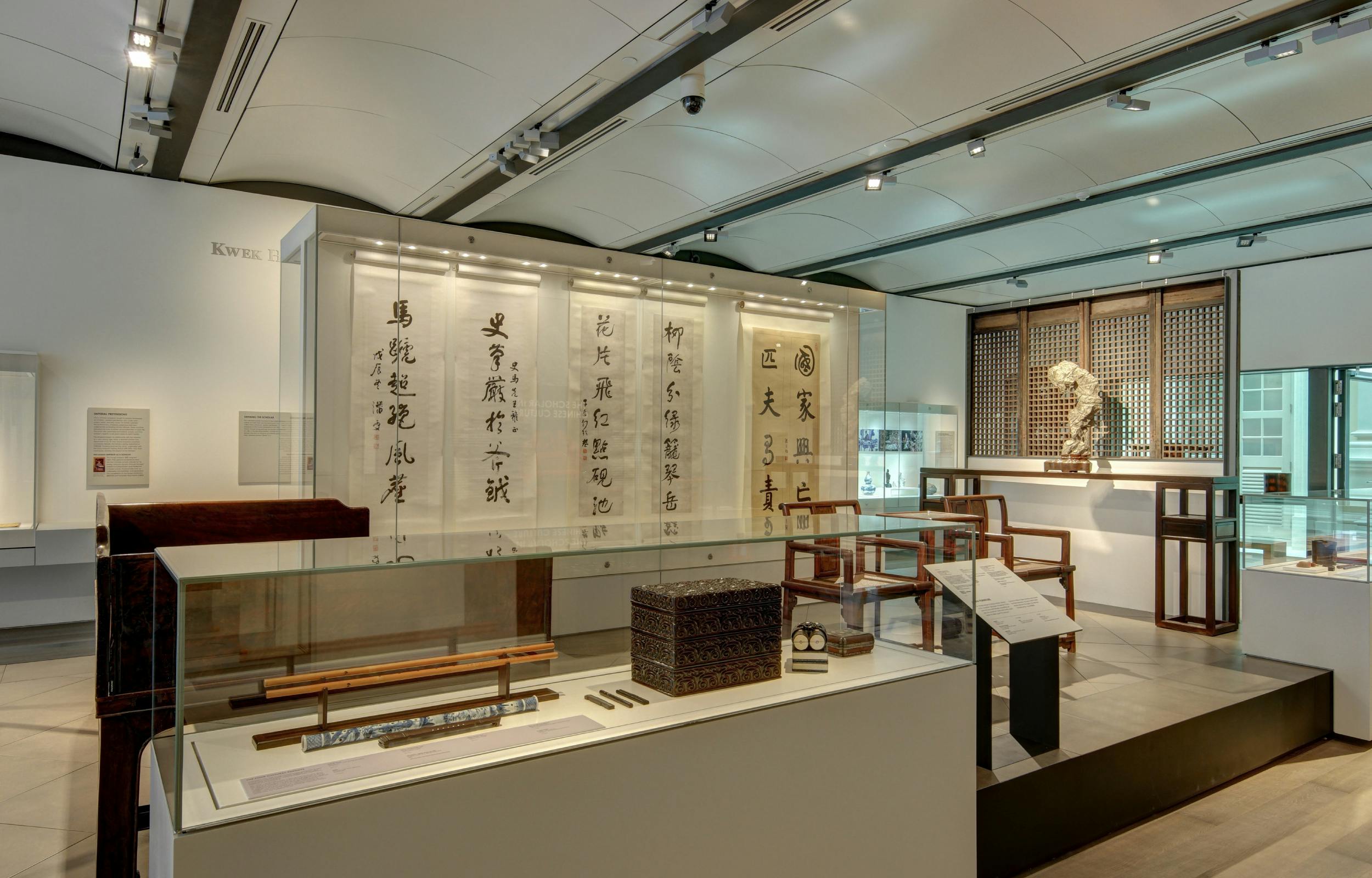 An exhibit showcasing calligraphy scrolls, traditional furniture, and artifacts in a well-lit museum setting.
